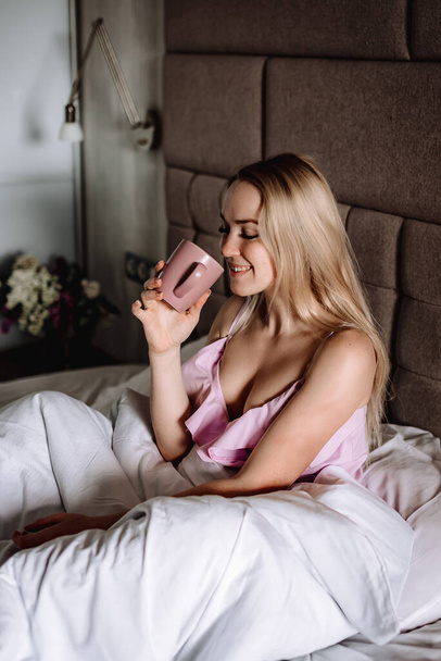 Dívka v posteli s šálkem kávy nebo čaje. Mladá žena se ráno probudí - Fotografie, Obrázek