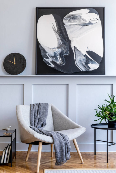 Stylish interior of living room with design grey armchair, plaid, marble stool, paintings, plant, decoration, black clock and elegant personal accessories in modern home decor. - Foto, afbeelding
