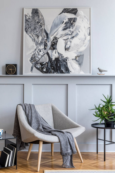 Stylish interior of living room with design grey armchair, pillows, coffee table, paintings, plant, decoration, black clock and elegant personal accessories in modern home decor. - 写真・画像