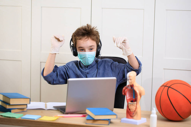 Etäopetus verkossa. koulupoika lääketieteellisessä naamiossa opiskelee kotona, työskentelee kannettavan tietokoneen muistikirjassa ja tekee koulun kotitehtäviä. sepelvaltimoviruksen karanteeni
 - Valokuva, kuva