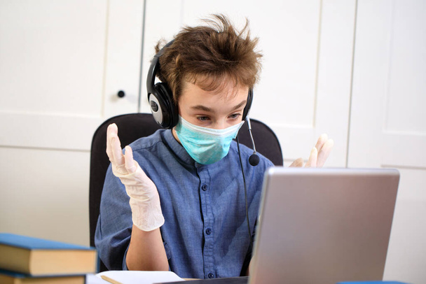 Distance learning online education. schoolboy in medical mask studying at home, working at laptop notebook and doing school homework. coronavirus quarantine - Photo, Image