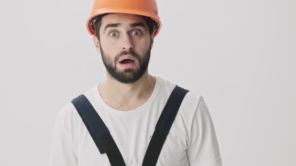 Shocked stressed young bearded man builder isolated over white wall background in helmet - Кадры, видео