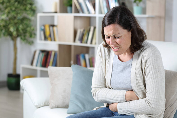 Middle age woman in pain suffering a stomach ache holding tummy sitting on the sofa at home - Foto, imagen