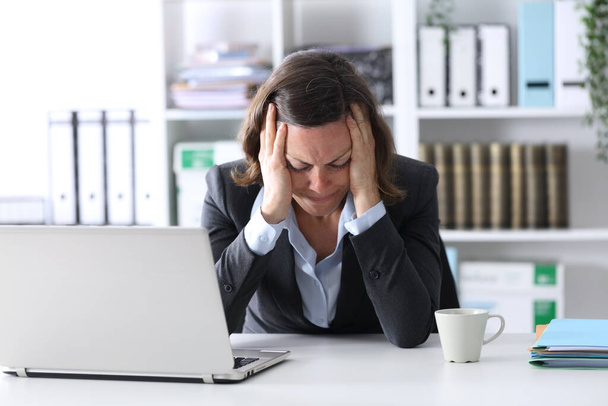 Sad adult executive woman with laptop complaining sitting on a desk at office - Valokuva, kuva