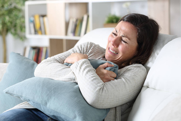 Sad adult woman crying sitting on the sofa holding pillow in the living room at home - Photo, Image