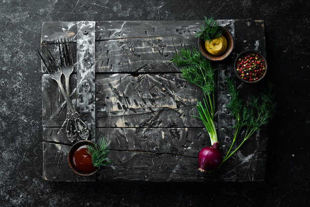Black kitchen background. Kitchen board, vegetables and spices on a black stone background. Top view. - Фото, изображение