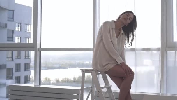 A sexy model poses at sunset in her apartment with panoramic windows. emotion evening mood calm, outside the city and the Dnieper river. - Video, Çekim