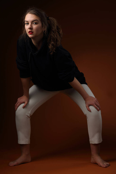 Studio portrait of a pretty teenage girl in a black hoodie and light colored sweatpants - Фото, зображення