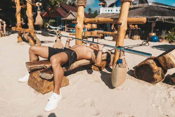 Muscle man training in eco gym on the beach. Wooden fitness equipment outside - Foto, Bild