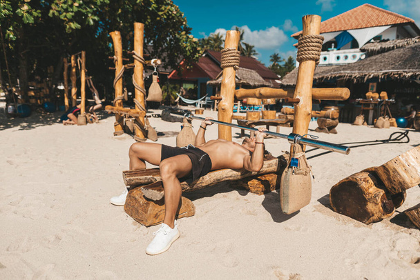 Muscle man training in eco gym on the beach. Wooden fitness equipment outside - Fotografie, Obrázek