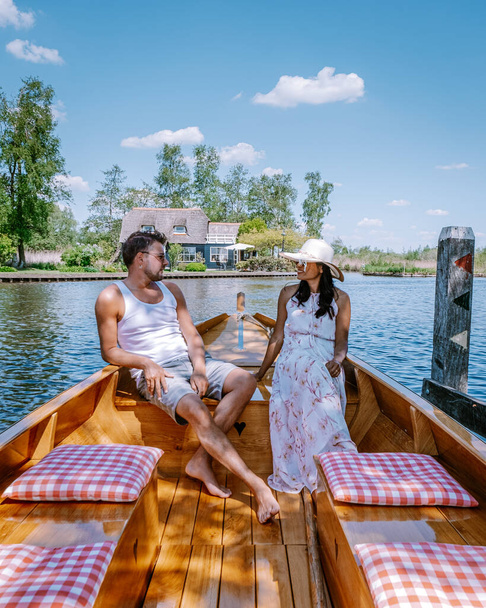 Giethoorn Netherlands couple visit the village with a boat ,view of famous village with canals and rustic thatched roof houses in farm area on a hot Spring day - Фото, изображение