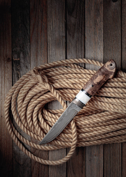 Hunter harci kézzel készített kés és kender kötél fából készült háttér. A penge felülete - maratás, kovácsolás nyomai. Fogantyú - japán juhar. - Fotó, kép
