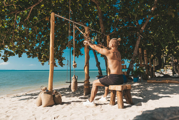 Muscle man training in eco gym on the beach. Wooden fitness equipment outside - Fotoğraf, Görsel
