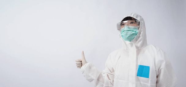 PPEスーツや個人的な保護機器や医療用ゴーグル、マスク、手袋、親指を表示するアジアの女性医師の広い角度画像や低パンデミックで幸せな瞬間を表す象徴的なそれのように  - 写真・画像