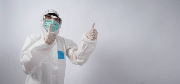 Широкий кут зображення азіатської жінки-лікаря в костюмі PPE або обладнання для особистого захисту і медичних окулярів, маска, рукавички і показуючи великий палець вгору або як символічні, які представляють щасливий момент з низькою пандемією  - Фото, зображення