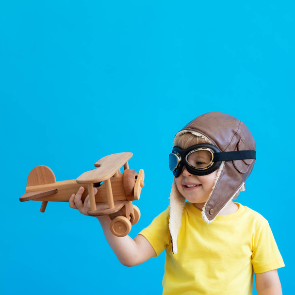 Gelukkige kind spelen met vintage houten vliegtuig. Hij heeft plezier tegen een blauwe achtergrond. Verbeelding en vrijheid - Foto, afbeelding