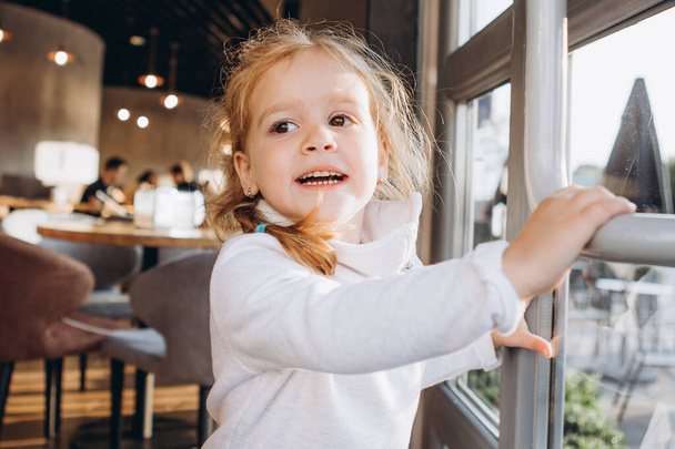 little playful girl opens the big glass door of a cozy cafe - Φωτογραφία, εικόνα