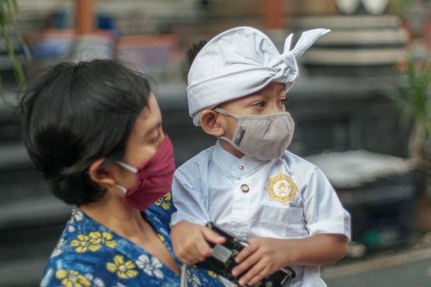 Балийская мать и ребенок одеты в балийскую традиционную одежду во время пандемии короны или ковида-19. Они оба используют маски, чтобы защитить себя от вирусных атак. - Фото, изображение
