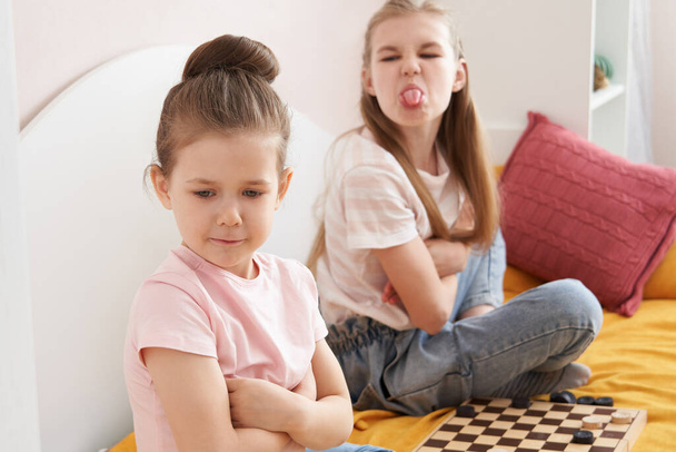 Two sisters playing checkers on a bad and having small fight - Photo, Image