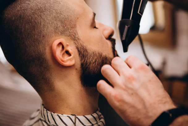Work in the Barber shop. Barber shaving a bearded man in a barber shop, close-up. Master cuts hair and beard  - Fotografie, Obrázek