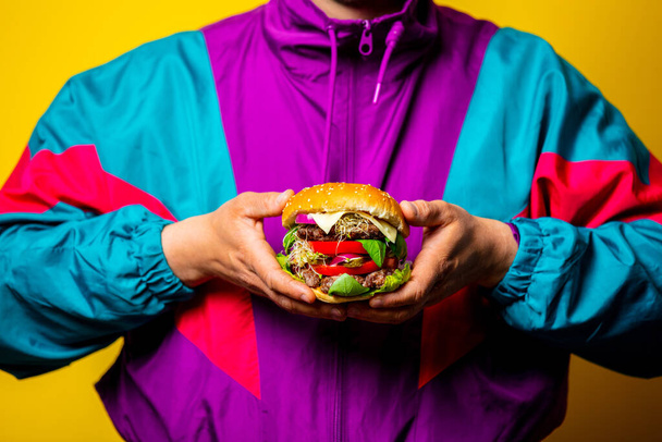 Style guy in 80s clothes with big burger on yellow background - 写真・画像