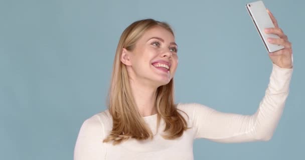 Portrait of a cheerful young girl with adorable smile taking selfie isolated over blue background - Video