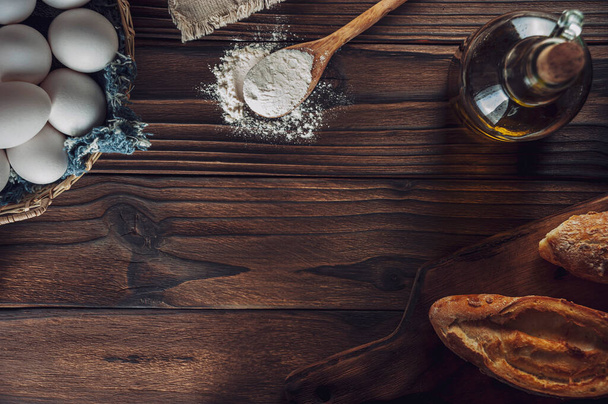 Кусок хлеба с маргарином, яйца в корзине и ложка с пшеничной мукой на деревянном столе
 - Фото, изображение