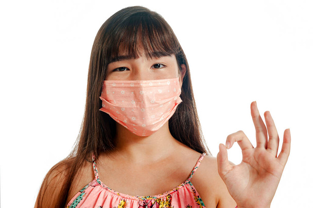 Asiática chica sonriendo, usando máscara y mostrando OK signo
 - Foto, Imagen