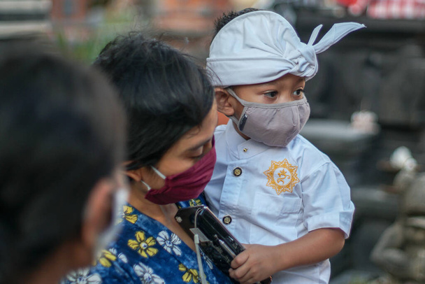 Mutter und Kind tragen während der Coronapandemie oder Covid-19 balinesische traditionelle Kleidung. Beide benutzen Masken, um sich vor Virenangriffen zu schützen. - Foto, Bild