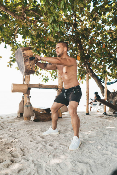 Muscle man training in eco gym on the beach. Wooden fitness equipment outside - Foto, Bild