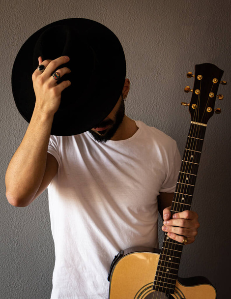 Young man with a guitar putting on a hat. Grey background. Selective focus. - Фото, зображення
