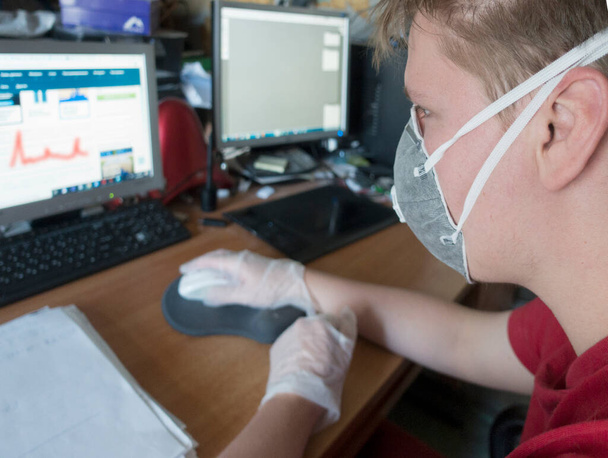 junger männlicher Programmierer, der mit Schutzmaske und Handschuhen am Computer arbeitet - Foto, Bild