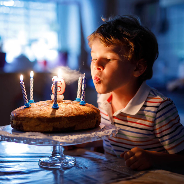 Adorable petit garçon blond joyeux célébrant son anniversaire. Enfants soufflant des bougies sur un gâteau fait maison, à l'intérieur. Fête d'anniversaire pour les écoliers, célébration familiale de 6 ans
 - Photo, image