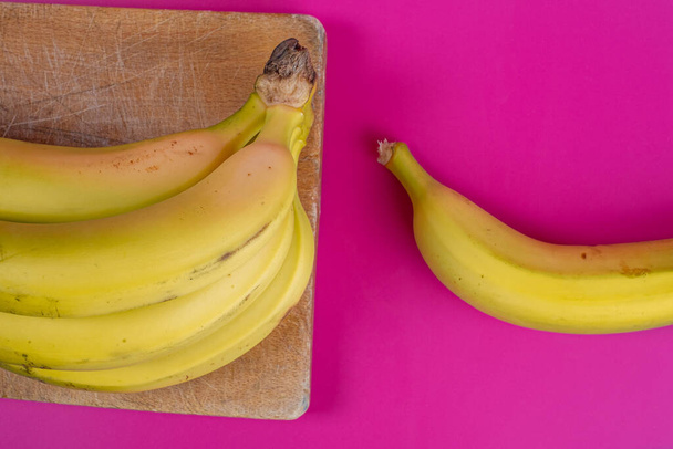 Bananen auf Holzbrett und Fuchsia-Hintergrund - Foto, Bild