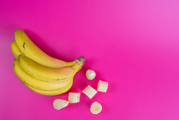 racimo de plátanos y plátano pelado sobre fondo fucsia
 - Foto, Imagen