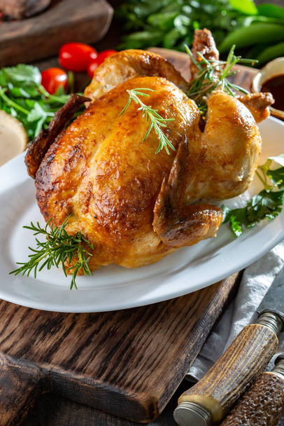 Целый жареный цыпленок на белой тарелке с розмарином, соусами и овощами
. - Фото, изображение