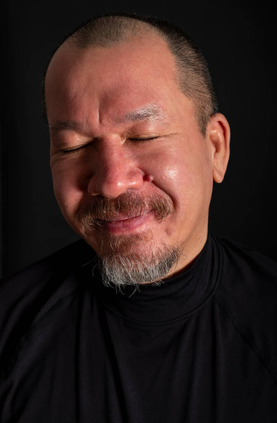 Studio portrét pohledné smíšené rasy muž s vousy usmívající se se zavřenýma očima, na černém pozadí - Fotografie, Obrázek