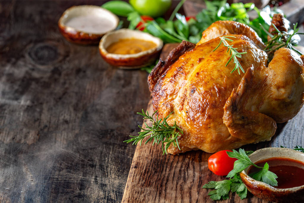 Whole Roasted Chicken on wooden board with rosemary, sauces and vegetables. - Фото, зображення