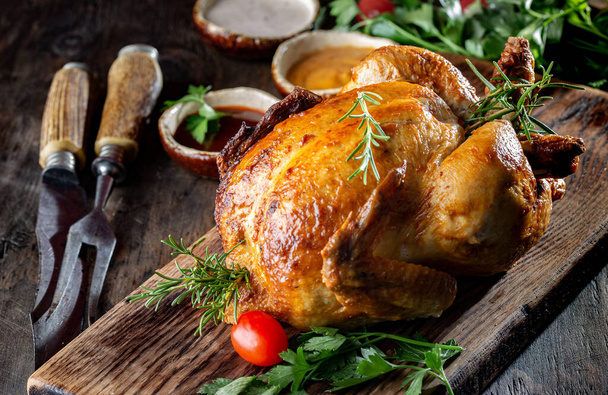 Whole Roasted Chicken on wooden board with rosemary, sauces and vegetables. - Фото, изображение