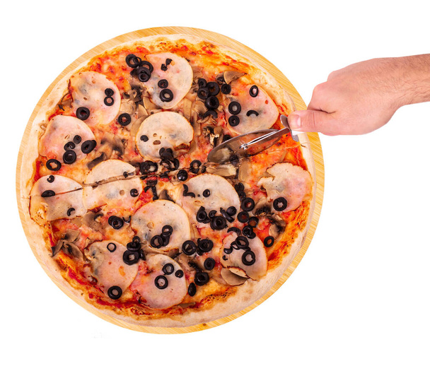 Le cuisinier coupe la délicieuse pizza au jambon, à la mozzarella, aux champignons et aux olives, avec un coupe-pizza sur un plateau en bois, isolé sur fond blanc, vue sur le dessus
 - Photo, image