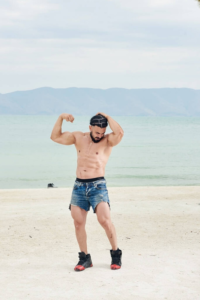 young man on the beach, young muscular man exercising on the beach, young muscular man doing bodibuilding exercises on the beach, athletic young man on the beach - Foto, immagini
