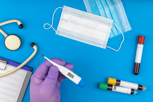 Composição de leigos planos com tubo de teste de sangue e termômetro eletrônico em fundo azul
 - Foto, Imagem
