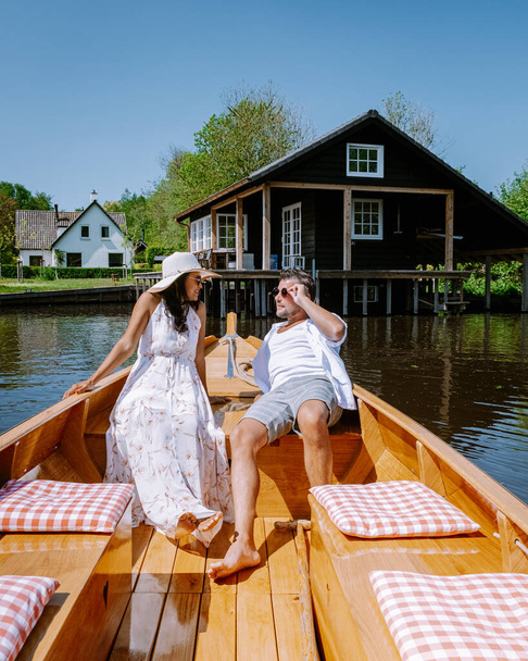 Giethoorn Hollandia pár látogasson el a faluba egy hajóval, kilátás nyílik a híres falu csatornák és rusztikus nádtetős házak tanyasi területen egy meleg tavaszi napon - Fotó, kép