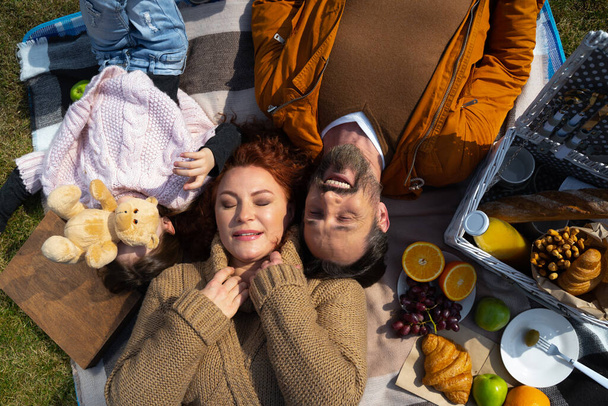 Happy family lying on blanket with food on sunny day - Foto, Bild