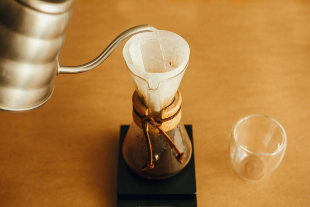 Alternative Kaffeezubereitung v60. Barista macht Filterkaffee auf braunem Hintergrund. Heißes Wasser aus Stahlkessel in Filter gießen, mit gemahlenem Kaffee auf der Waage übergießen. - Foto, Bild
