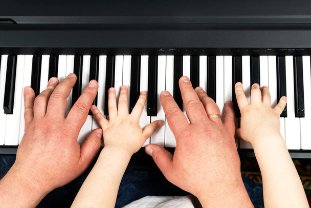 Руки дорослого чоловіка і маленької дитини грають на піаніно. Вчимося грати на піаніно. Навчання вдома. Залишитися вдома
. - Фото, зображення