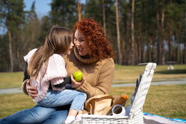 Cheerful mother and cute daughter having picnic outside the city - Foto, Imagen