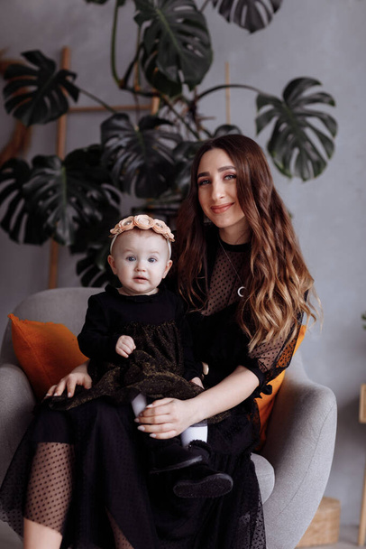 Beautiful mother sits on a chair and keeps her daughter on lap at home. family look concept. mother's, baby's day - Фото, зображення