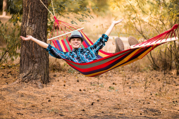 Joven feliz hombre libre en sombrero relajante al aire libre en hamaca en el bosque de otoño
 - Foto, imagen
