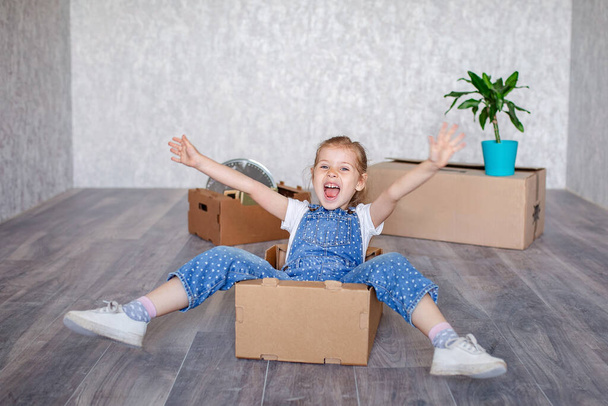 Ein kleines blondes Mädchen spielt zu Hause in Quarantäne mit Pappkartons. Das Kind zieht in eine neue Wohnung, ist glücklich und glücklich. - Foto, Bild